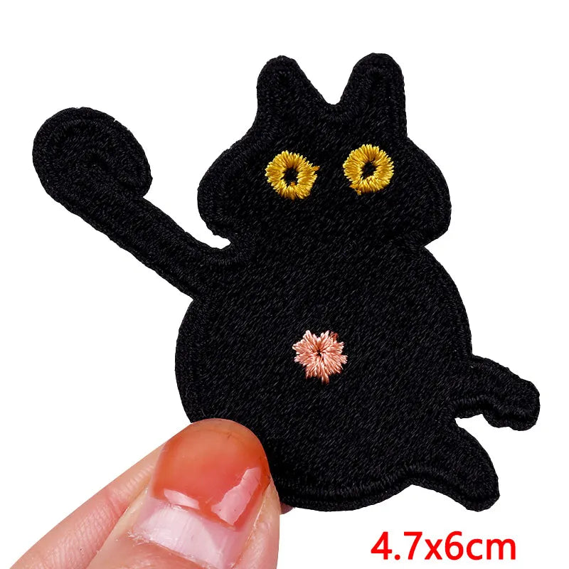 Black cat-shaped patch with yellow eyes and a pink nose, held by a hand to show size.