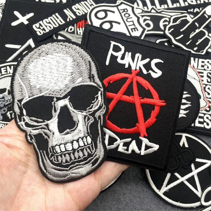 Collection of patches including a skull and anarchy symbol patch held by a hand.