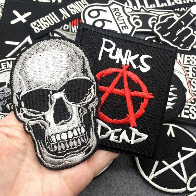 Collection of patches including a skull and anarchy symbol patch held by a hand.