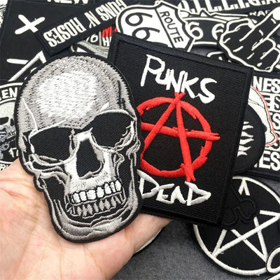Collection of patches including a skull and anarchy symbol patch held by a hand.