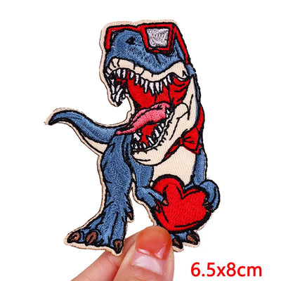 Embroidered patch of a dinosaur holding a heart, held by a hand on a white background.