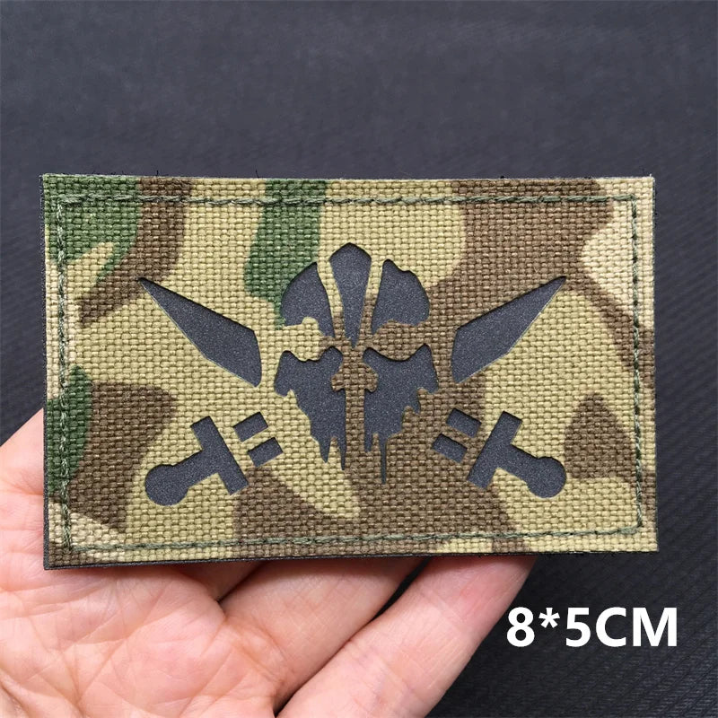 Camouflage patch with a black symbol held in a hand against a dark background