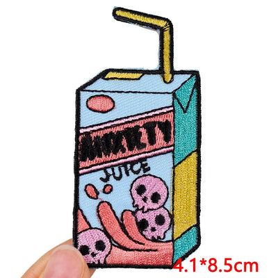 Embroidered patch of a juice box with cartoon skulls and a straw on a white background.