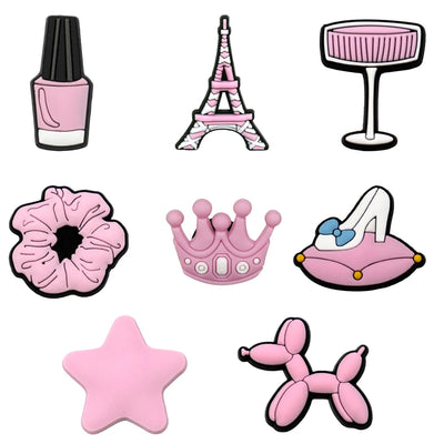 Set of pink-themed shoe charms including a nail polish, Eiffel Tower, glass, scrunchie, crown, high heel, star, and balloon dog on a white background.