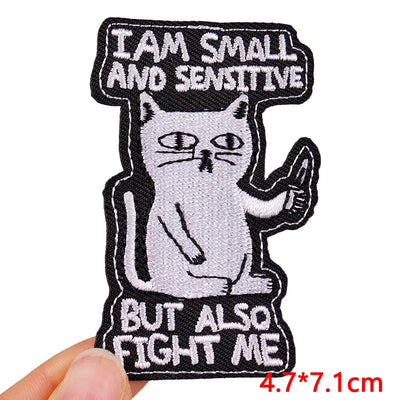 Embroidered patch with a cat holding a sign saying 'I am small and sensitive but also fight me' held by a hand.