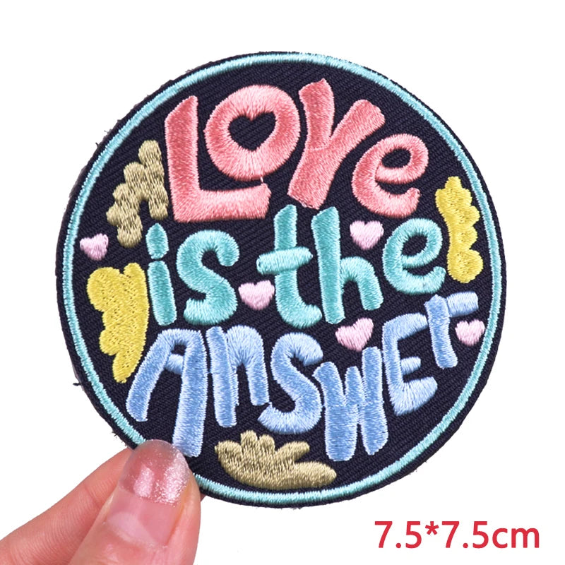 Circular patch with 'Love is the Answer' text held by a hand, on a white background.