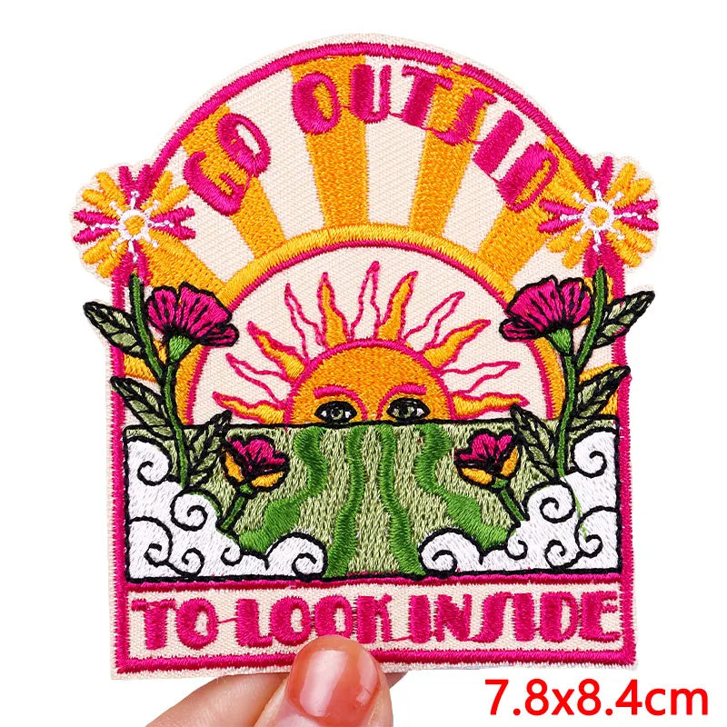 Embroidered patch with sun and flowers design held by a hand, text 'GO OUTSIDE TO LOOK INSIDE'.