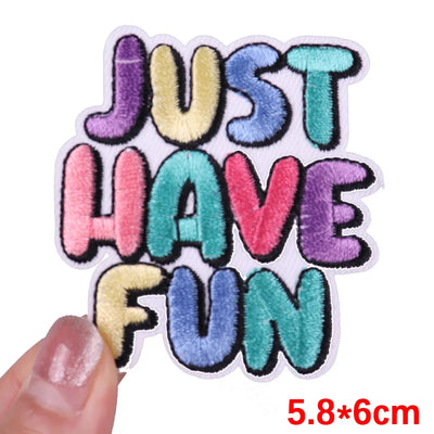 Colorful patch with 'JUST HAVE FUN' text held by a hand on a white background
