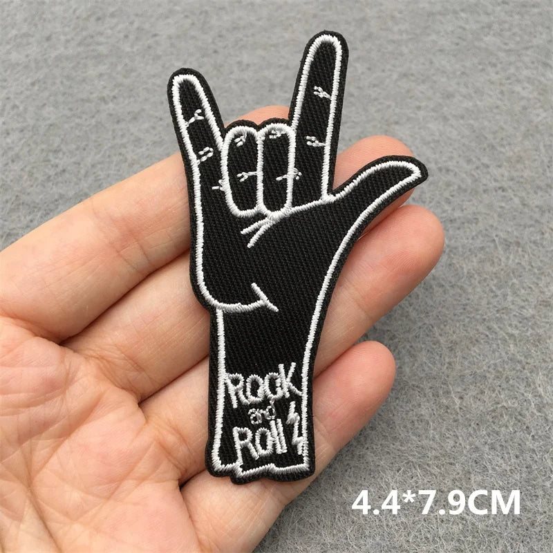 Hand holding a black and white embroidered patch of a hand making a rock and roll sign.