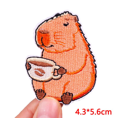 Patch of a capybara holding a coffee cup with a hand holding it, on a white background.