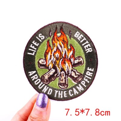 Round patch with campfire design and text 'Life is better around the campfire' held by a hand.