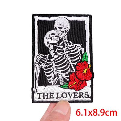 Patch with skeletons embracing and red flowers labeled 'The Lovers' held by a hand.