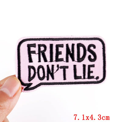 Patch with 'FRIENDS DON'T LIE' text held by a hand on a white background