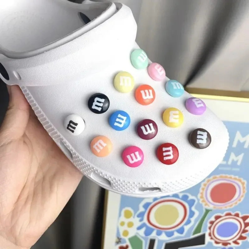 White sandal with colorful M&M buttons held by a hand, with a colorful book in the background.