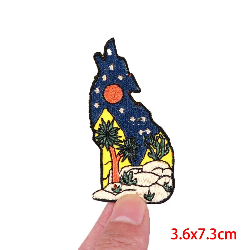 Decorative patch of a wolf silhouette with a starry night sky held between fingers.