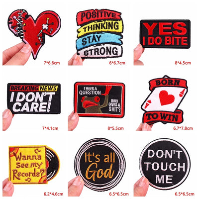 Collection of various patches with different designs and text, held by hands against a white background.