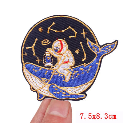 Embroidered patch of an astronaut on a whale with star constellations, held by a hand.
