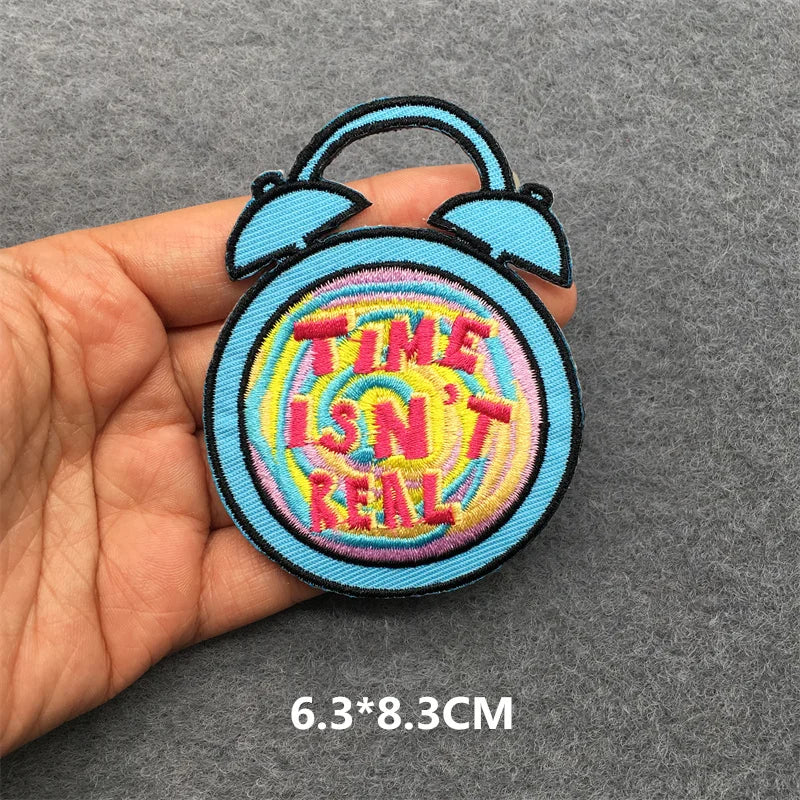 Colorful patch with 'TIME ISN'T REAL' text held by a hand on a gray background