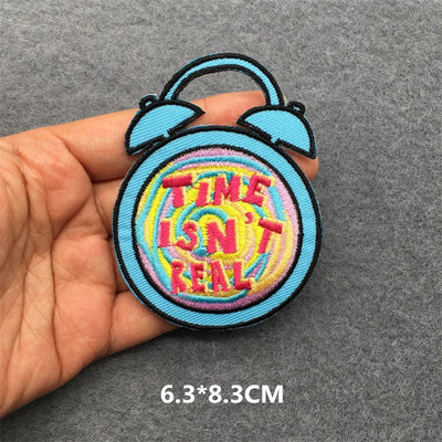 Colorful patch with 'TIME ISN'T REAL' text held by a hand on a gray background