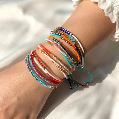 Wrist with multiple colorful beaded bracelets on a light background