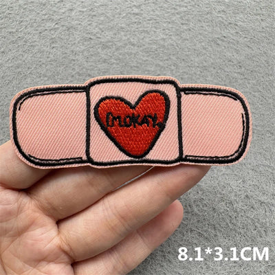 Patch with heart and text held by a hand on a gray background