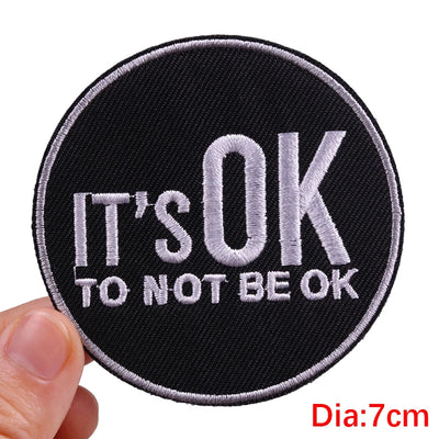 Round patch with 'It's OK To Not Be OK' text held by a hand on a white background