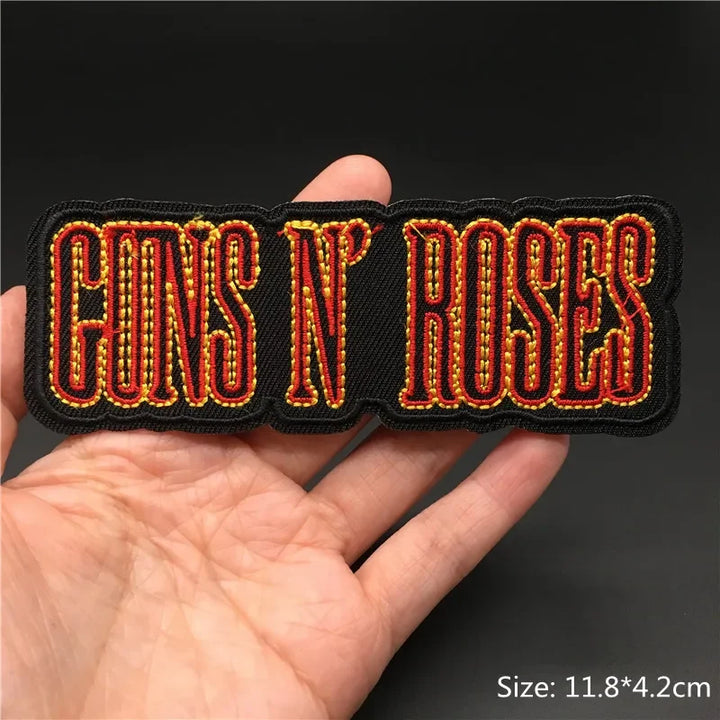 Hand holding a black red and gold Guns N’ Roses embroidered iron-on patch 11.8x4.2cm on a dark background