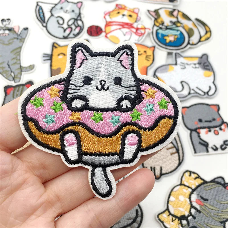 Embroidered patch of a cat on a donut held by a hand, with more cat-themed patches in the background.