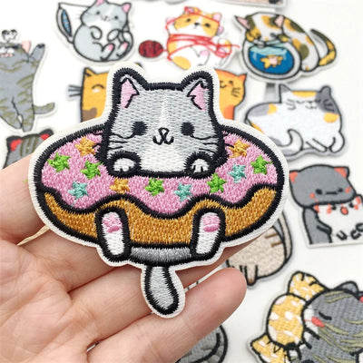 Embroidered patch of a cat on a donut held by a hand, with more cat-themed patches in the background.
