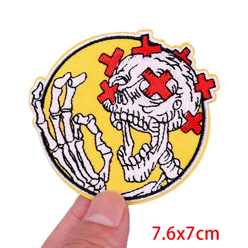 Embroidered patch with skeleton design and red crosses on a yellow background, held by a hand.