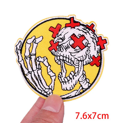 Embroidered patch with skeleton design and red crosses on a yellow background, held by a hand.