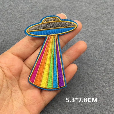Colorful UFO patch held in a hand with a gray background