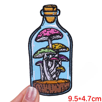 Embroidered patch of mushrooms in a bottle held by a hand with measurement text.