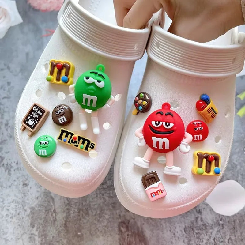 White clogs with colorful M&M-themed charms on a gray surface