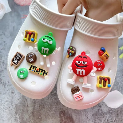 White clogs with colorful M&M-themed charms on a gray surface