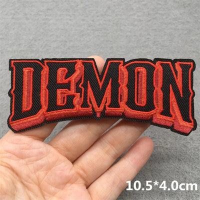Embroidered patch with 'DEMON' text held in a hand against a gray background