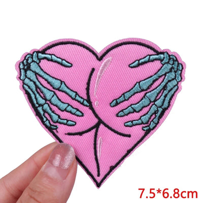 Heart-shaped patch with skeleton hands holding it, held by a hand on a white background.