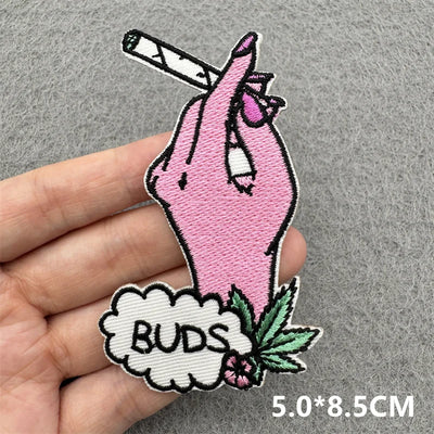Embroidered patch of a pink hand holding a joint with 'BUDS' text, held by a hand on a gray background.
