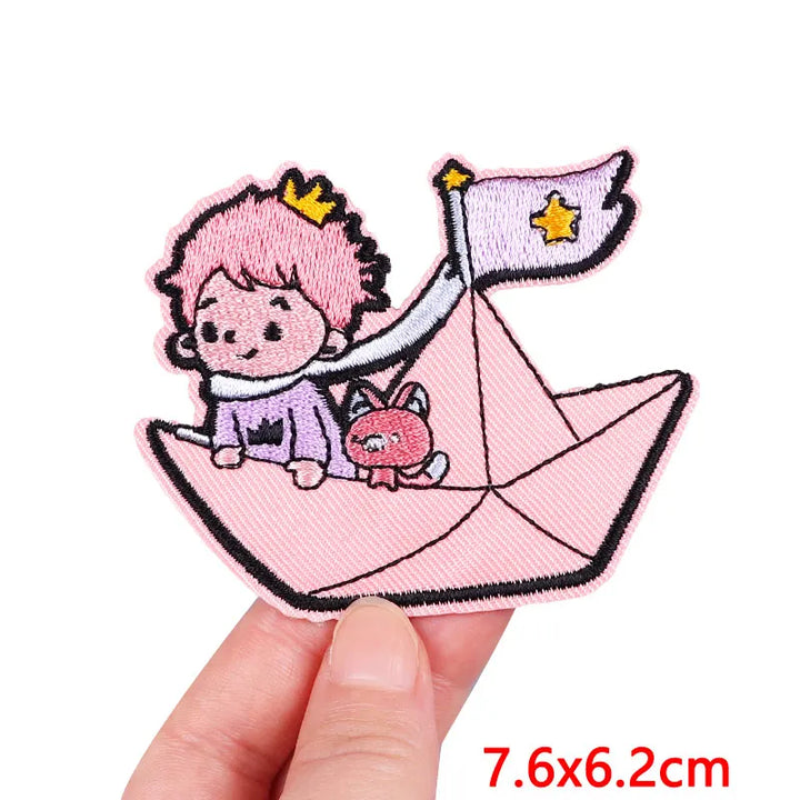 Embroidered patch of a girl with pink hair and a cat on a pink paper boat held by a hand.