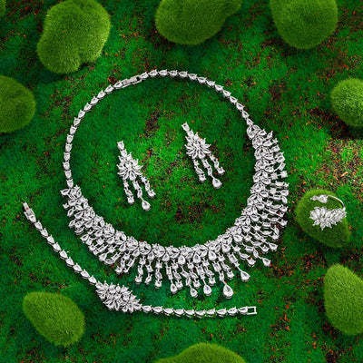 Silver jewelry set including necklace, earrings, bracelet and ring on a green textured background