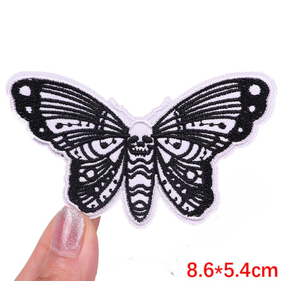 Black butterfly patch held by a hand with measurement text on a white background