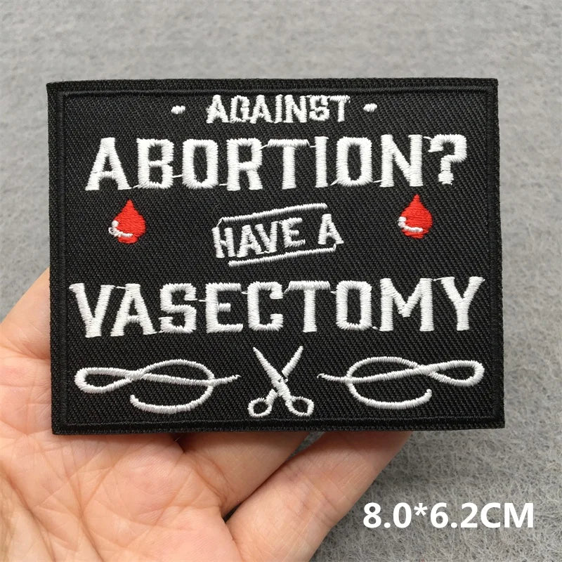 Embroidered patch with text 'Against abortion? Have a vasectomy' held by a hand on a gray background.
