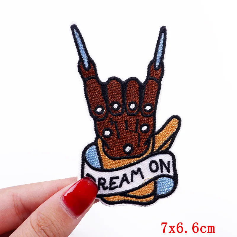 Handmade patch with 'Dream On' banner held by a hand with red nail polish on a white background.