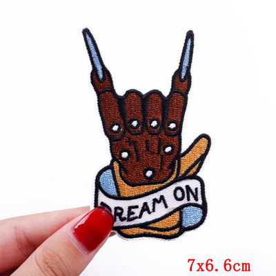 Handmade patch with 'Dream On' banner held by a hand with red nail polish on a white background.