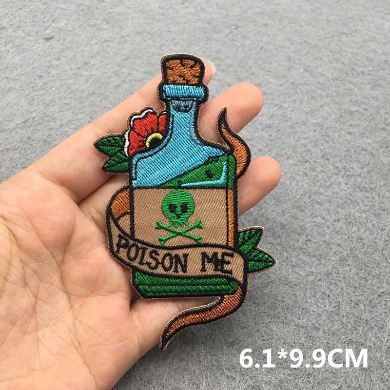 Embroidered patch of a bottle labeled 'Poison Me' held by a hand on a gray background.