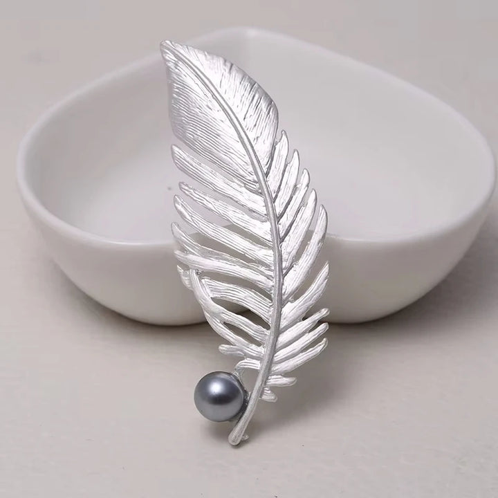Silver feather-shaped brooch with a pearl on a light background