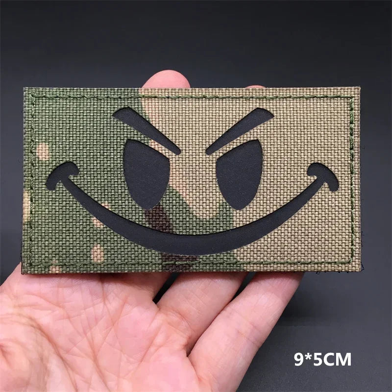 Green patch with a black smiley face design held in a hand against a dark background