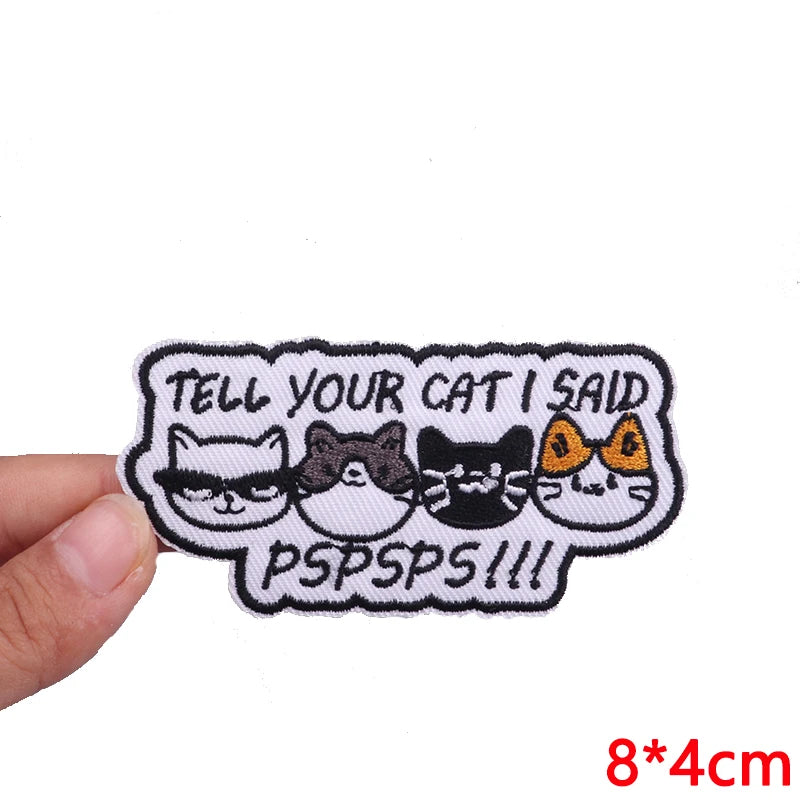 Embroidered patch with cartoon cats and text held by a hand on a white background