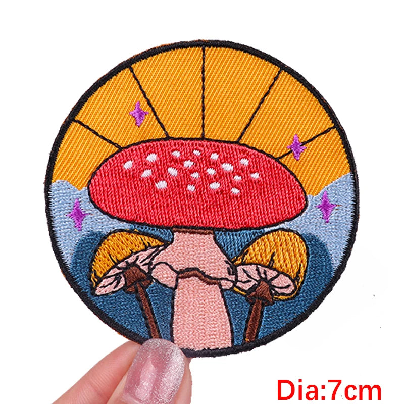 Circular embroidered patch with a red mushroom design held by a hand, against a white background.