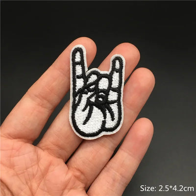 Hand holding a black and white embroidered patch of a hand making a peace sign.